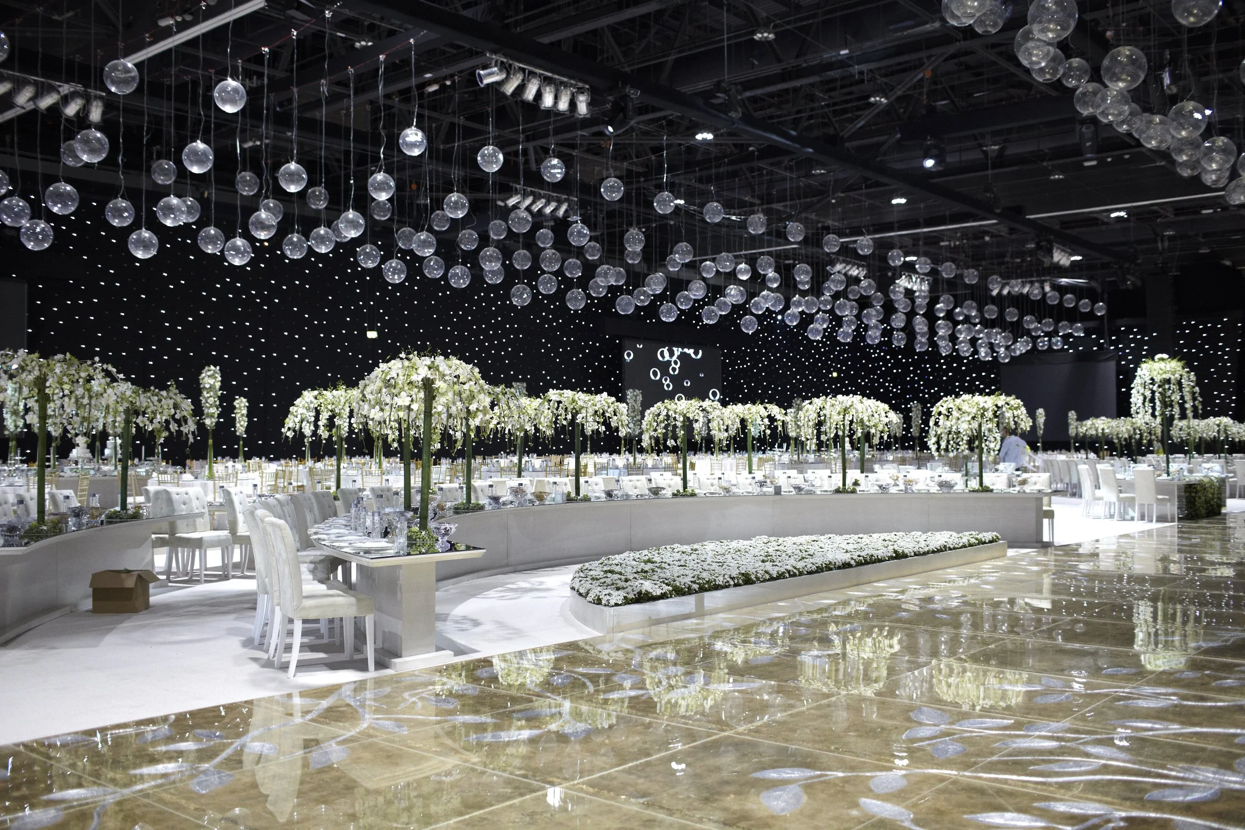 Modern wedding reception with white orchid trees, hanging glass globes, and starry black ceiling by Daniel Ost.