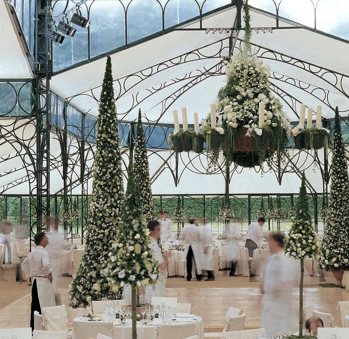 Classic white wedding with tall floral trees and candlelit chandelier in a glass pavilion by Daniel Ost.