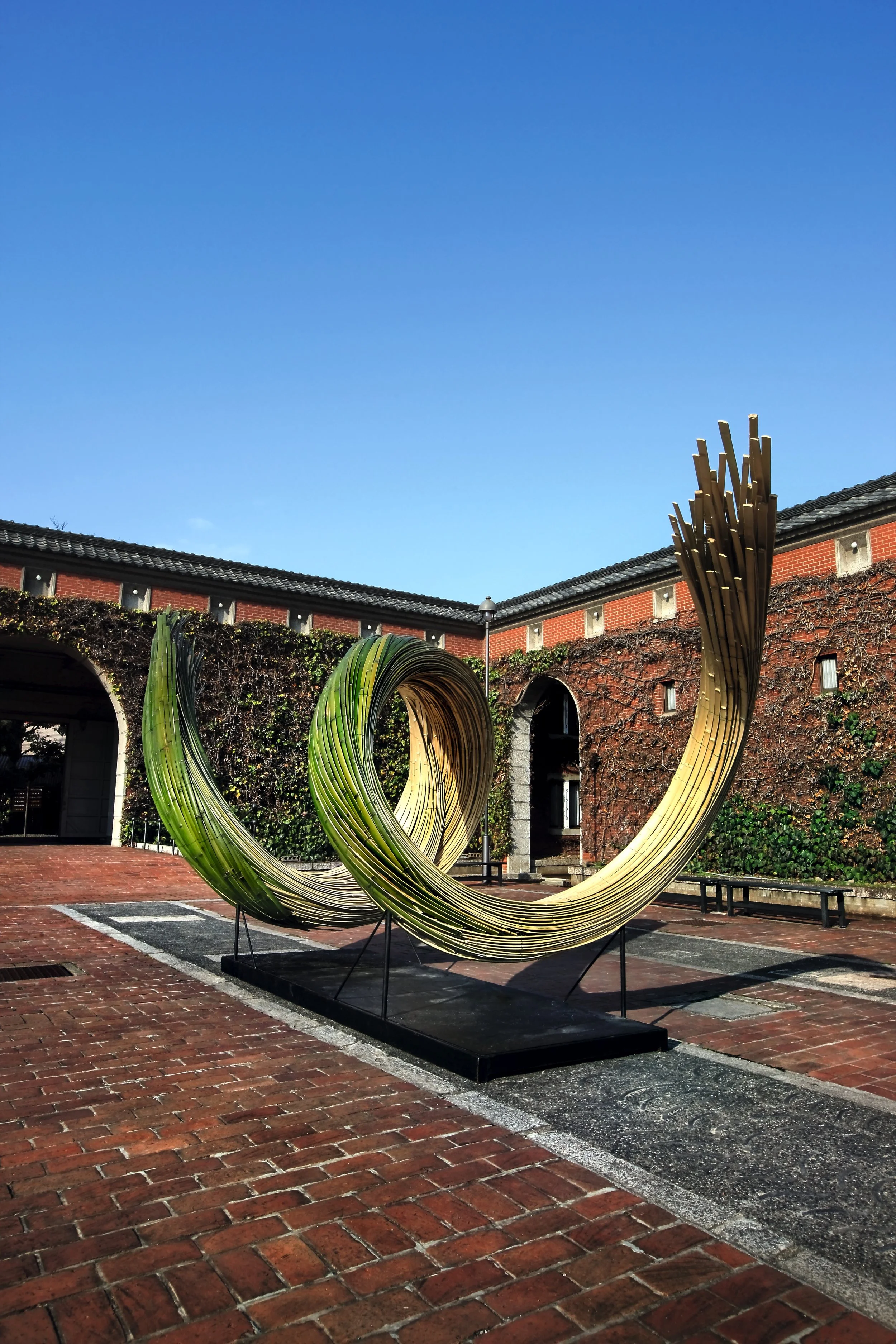Large-scale outdoor floral sculpture with curved bamboo arcs, blending natural artistry with architectural design in a courtyard.