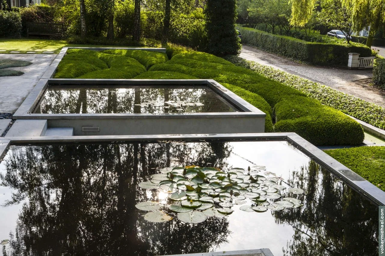 Minimalist private garden with rectangular reflecting pools, lily pads, and manicured boxwood hedges in a structured modern layout.