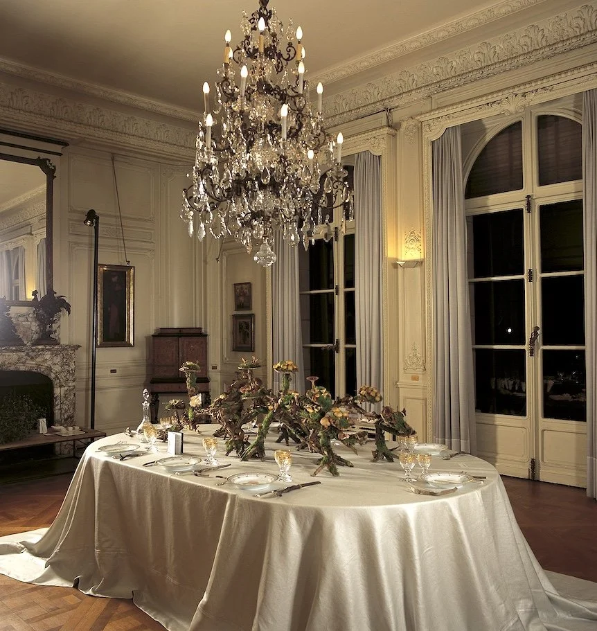 Long table set with refined floral arrangements beneath a crystal chandelier, creating a sophisticated and intimate wedding reception setting.