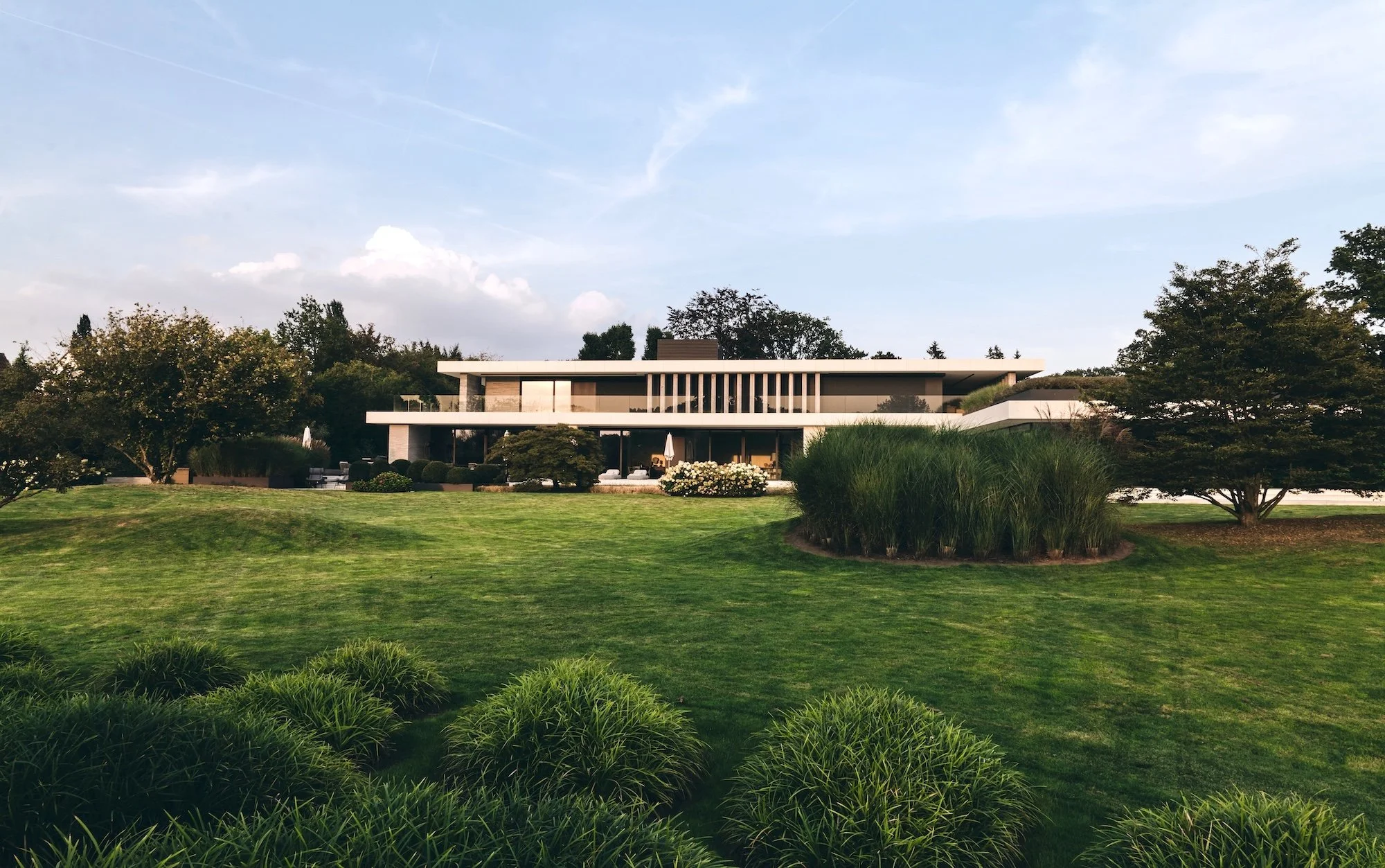 Modern private estate with expansive lawn, sculptural grasses, and a sleek villa set in a landscaped parkland.