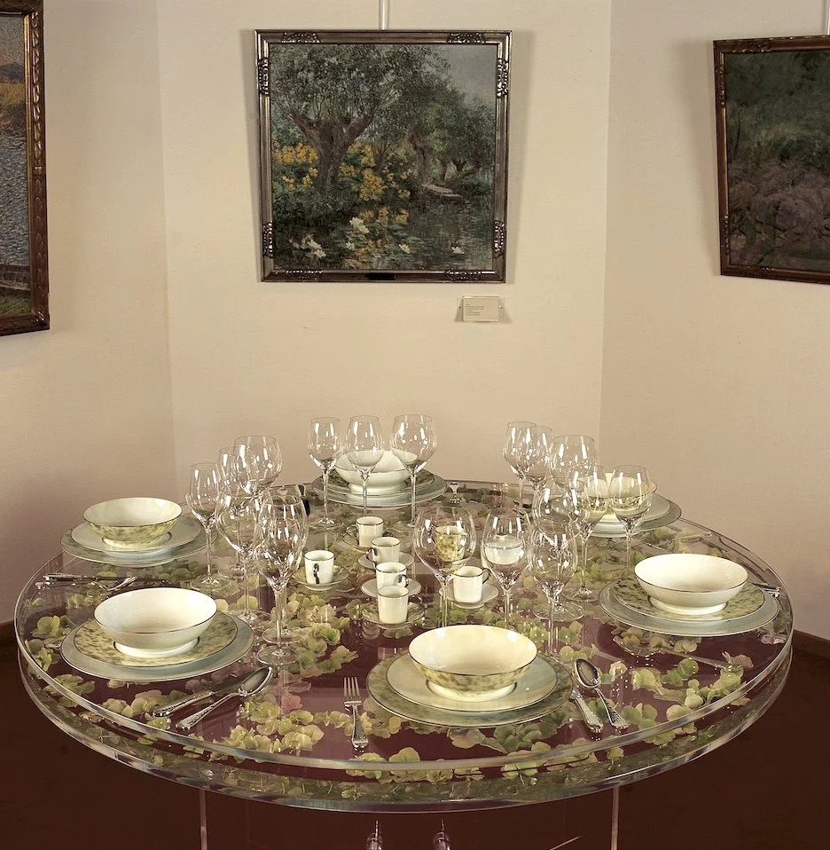 Round dining table featuring delicate flowers encased beneath a glass surface, paired with fine tableware for a refined wedding dinner.