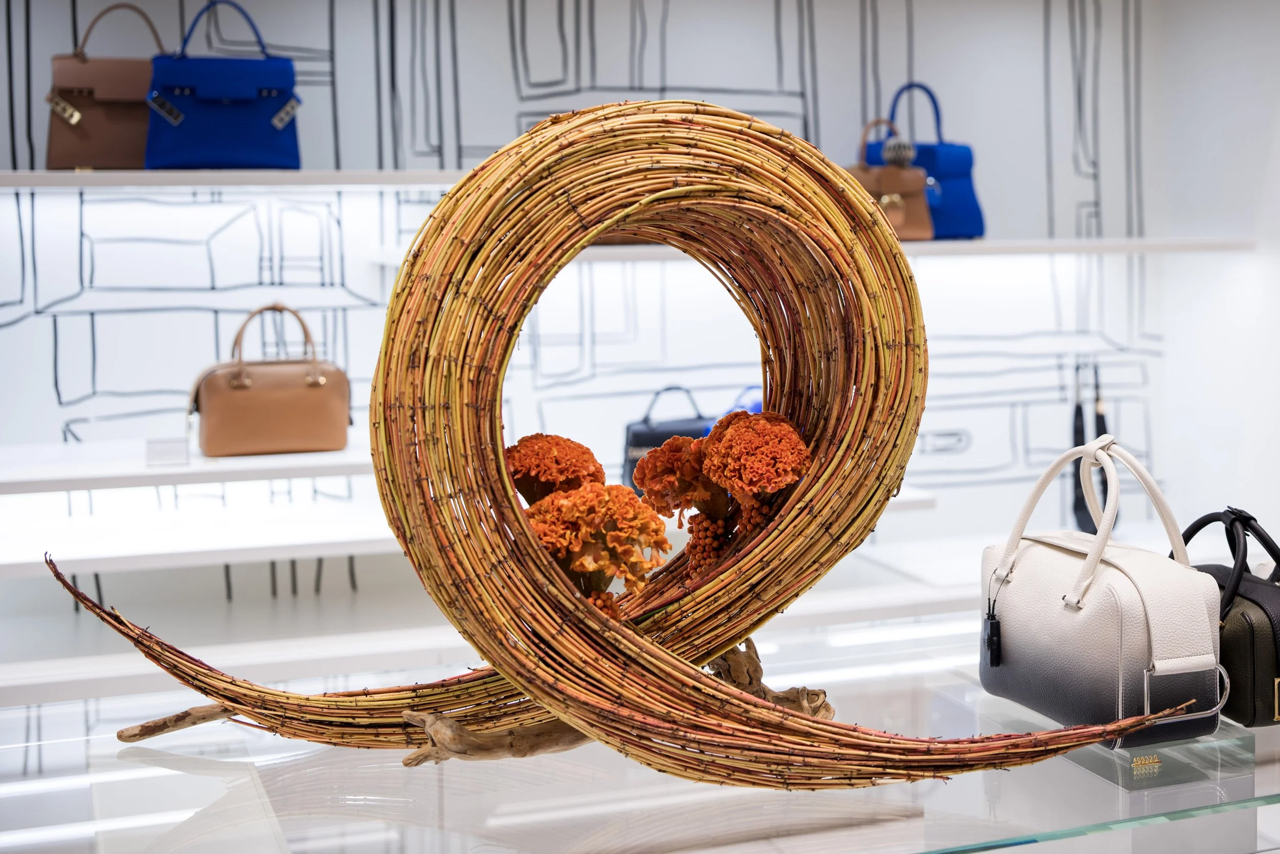 Store display with a decorative woven sculpture and handbags in the background.