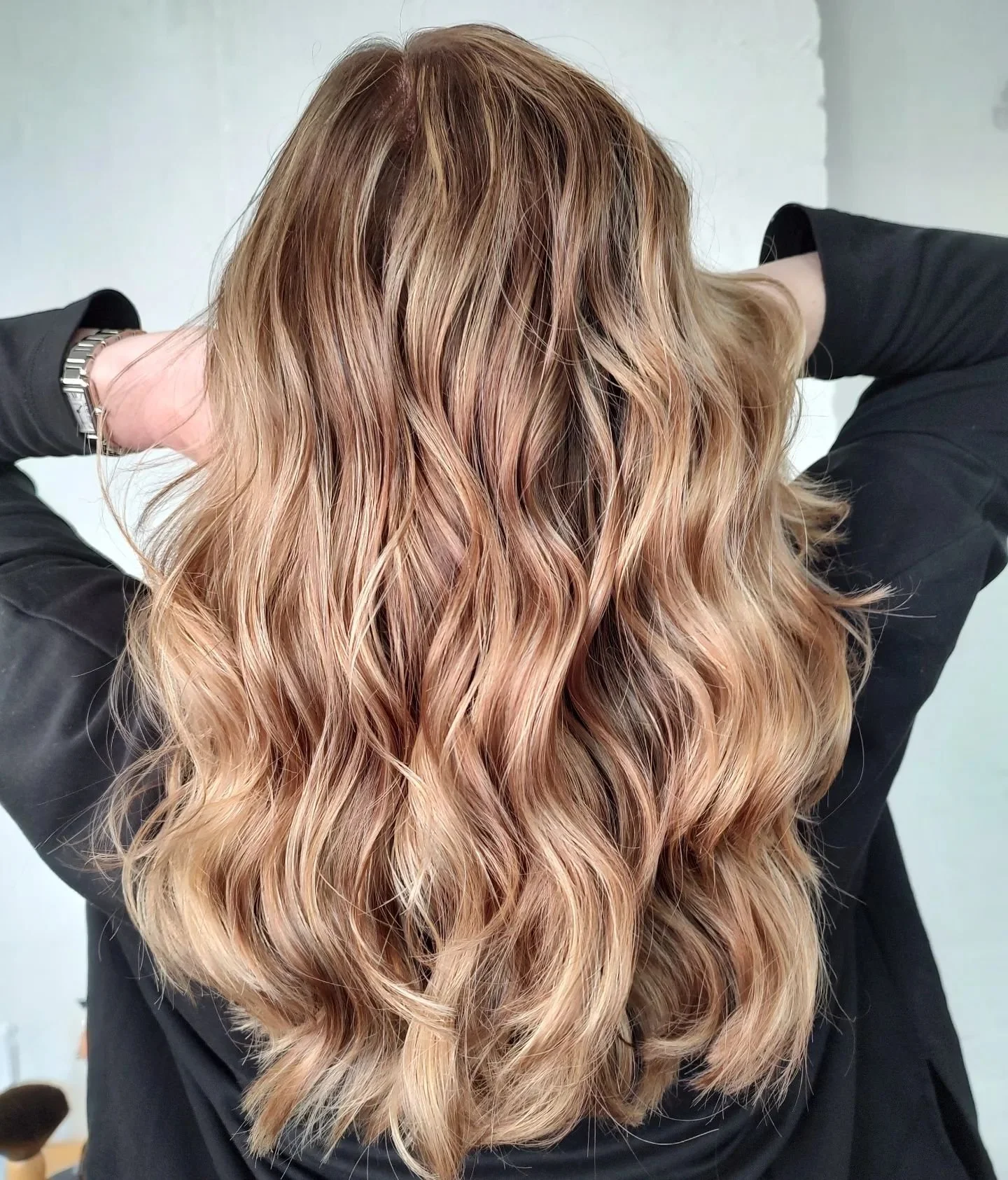 Woman with long, wavy, copper-colored hair, wearing a black long-sleeve shirt, holding her hair up behind her head.