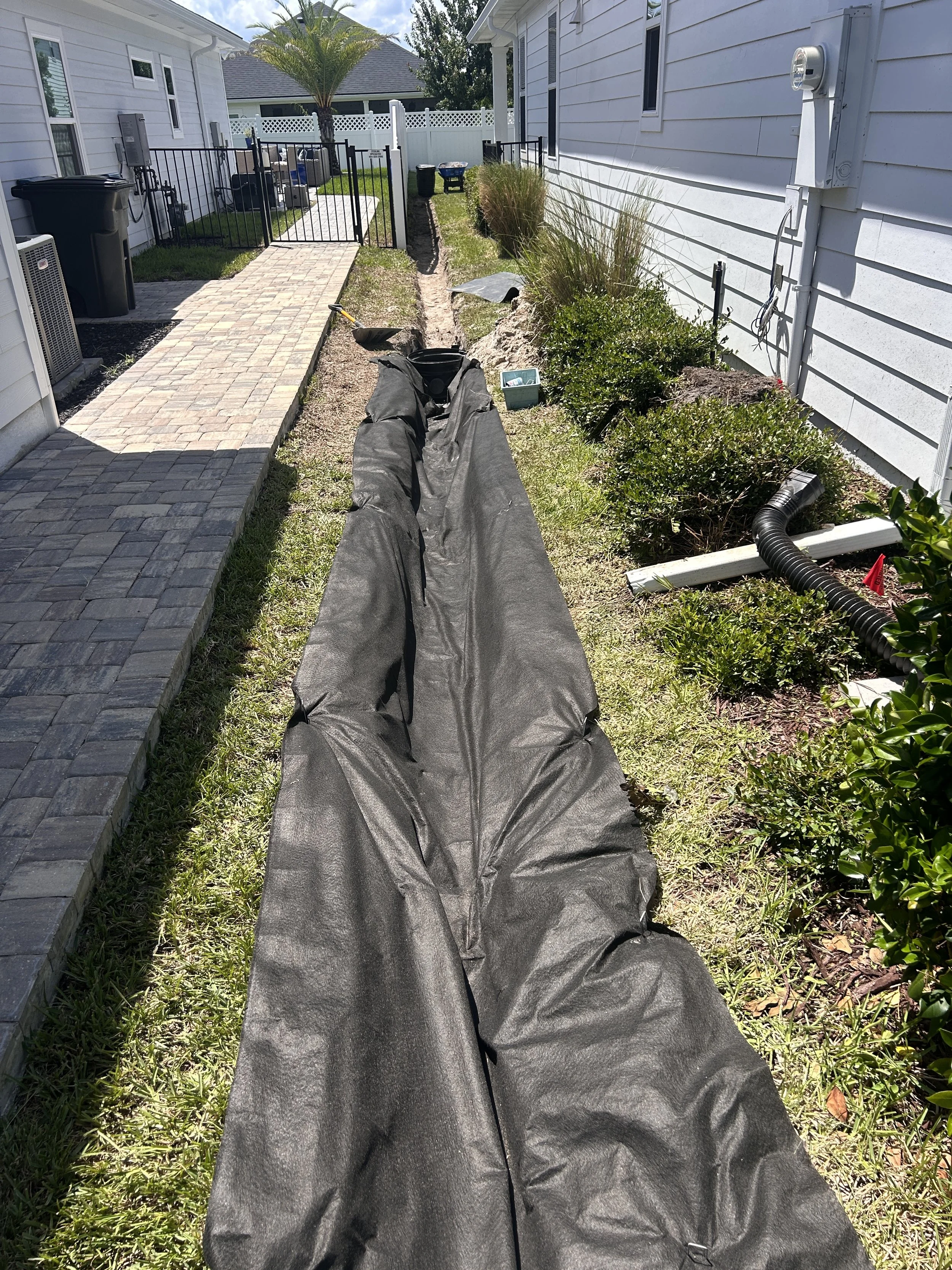 Long trench covered with black geotextile fabric for underground drainage system.