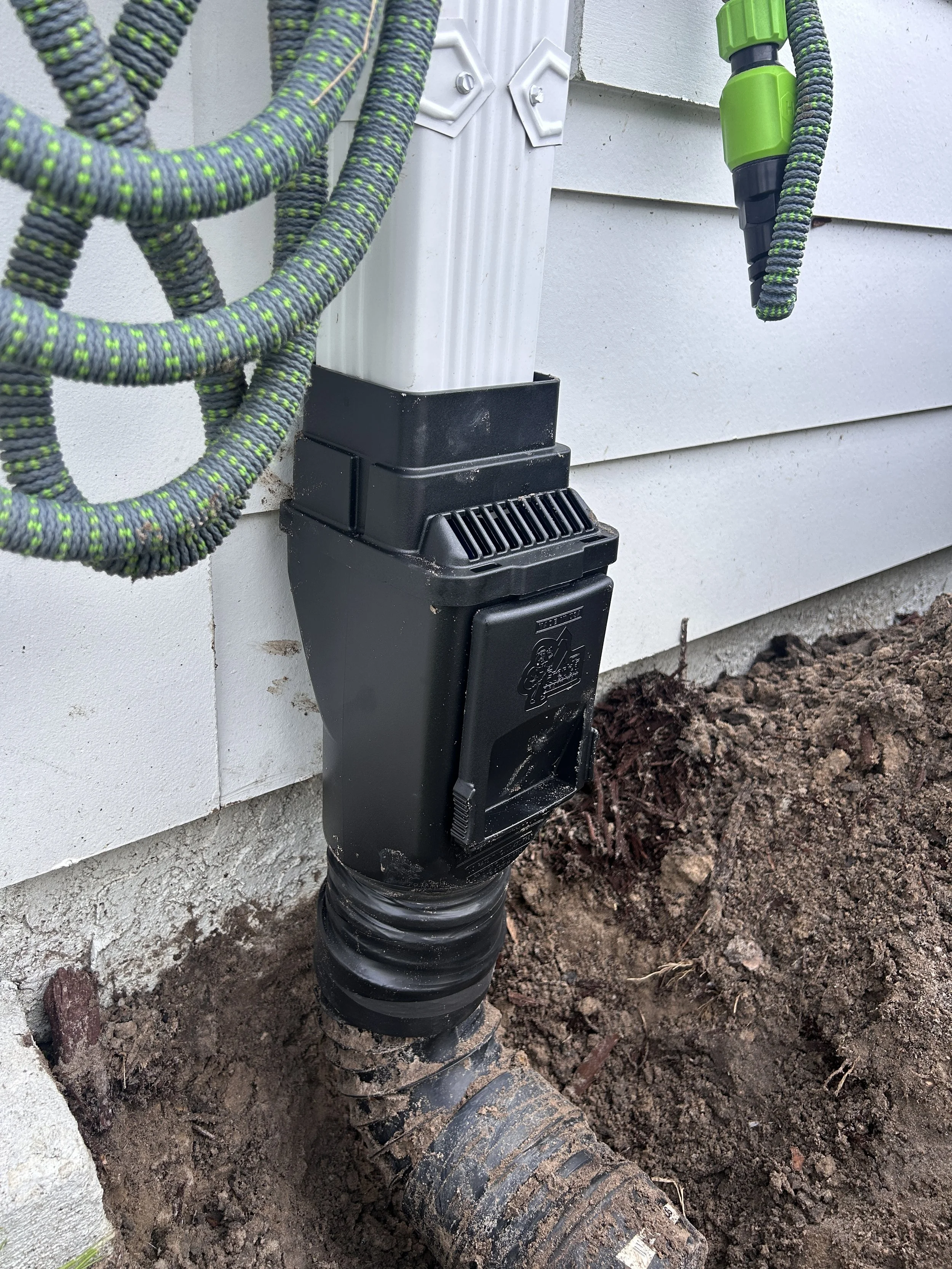 Surface drain installation on the side of a house, with a black pipe connected directly to the rainwater system.