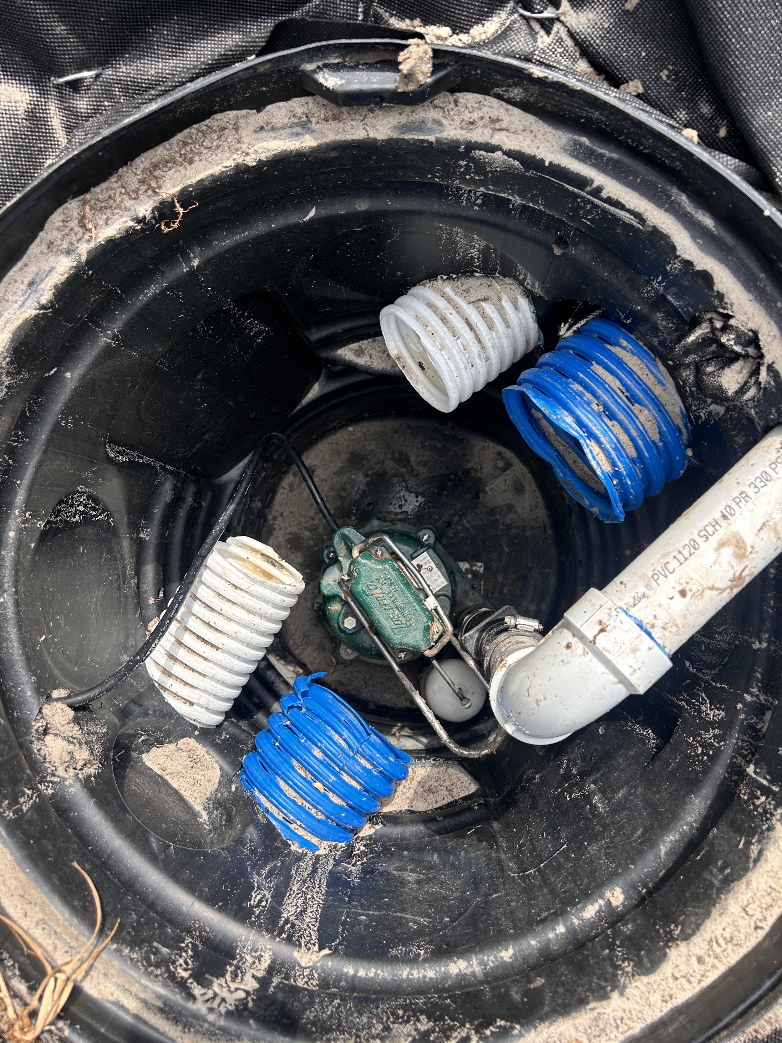 Inside view of sump pump system with PVC and flexible drainage pipes.
