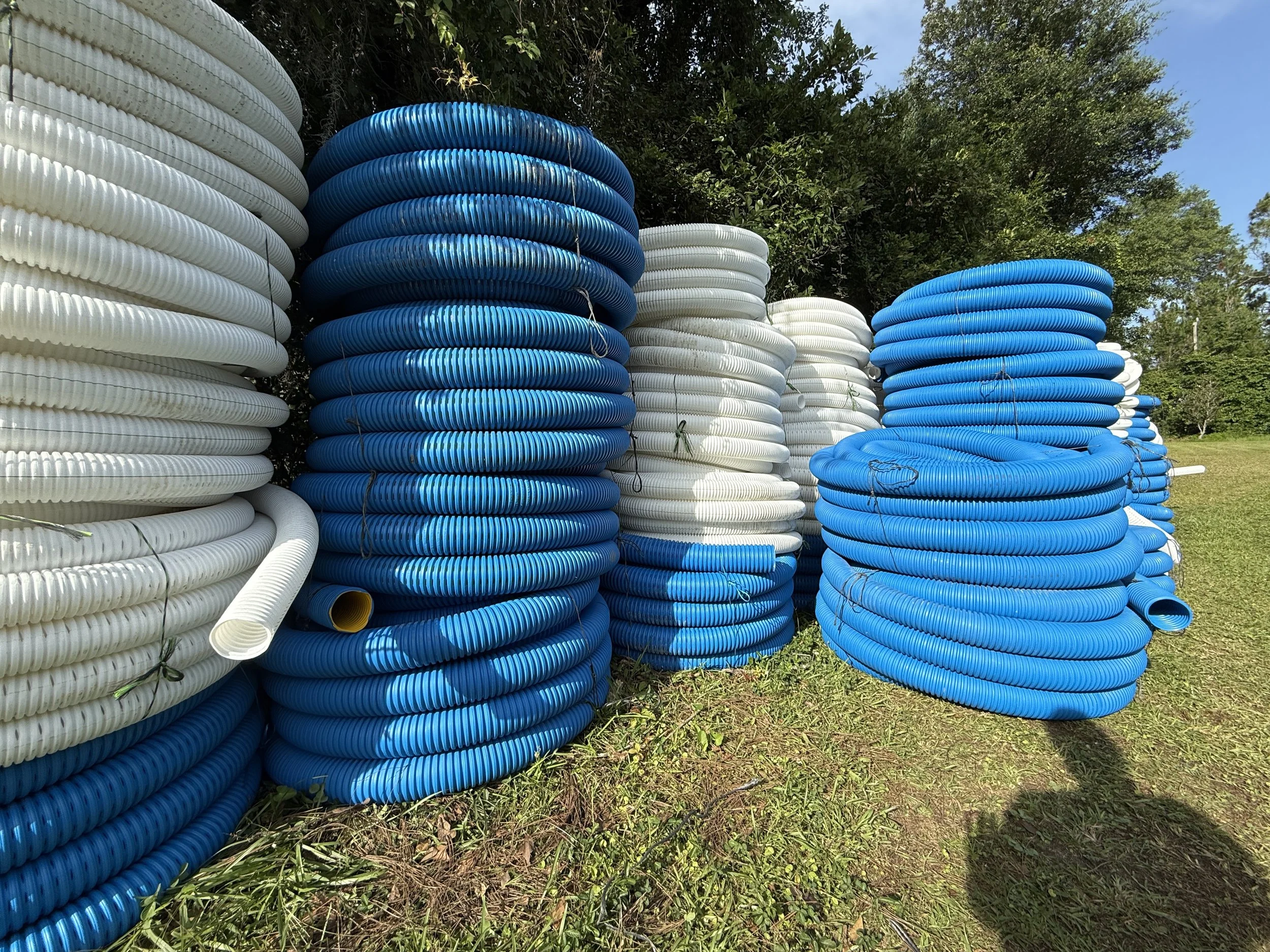 Rolls of blue and white corrugated drainage pipes stacked outdoors, ready to be used for drainage projects.