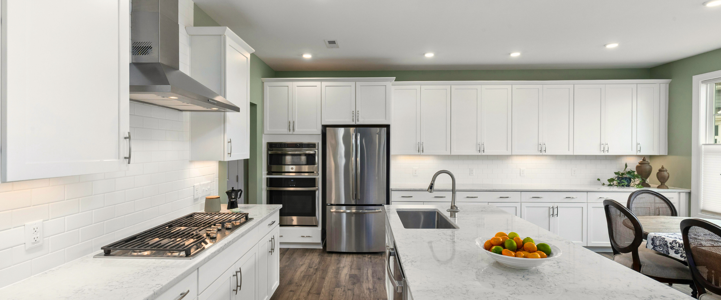Modern white kitchen with stainless steel appliances and a large island with a bowl of oranges and limes.