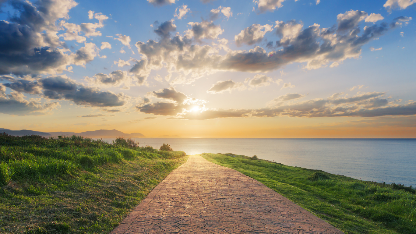 A stone path leads through green hills toward the ocean at sunset, symbolizing an open path forward in recovery.