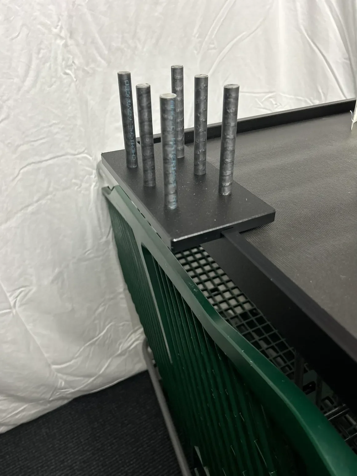 Six black cylinders with blue text on a black platform on a table with a black surface and a white textured wall in the background.