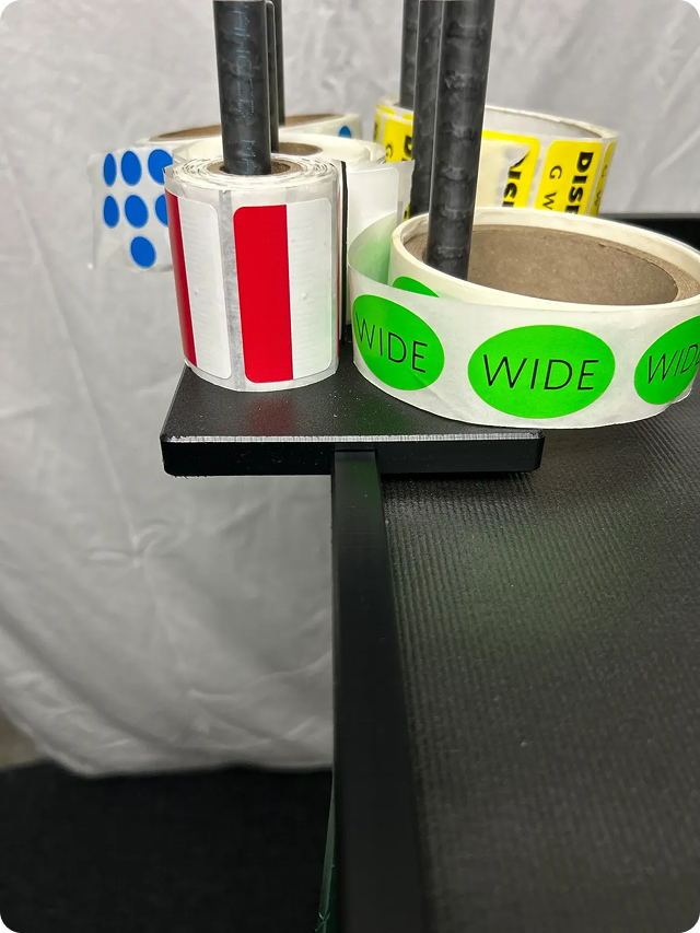 Rolls of adhesive and duct tape with black pencils or pens inserted, placed on a black surface with a gray textured background.