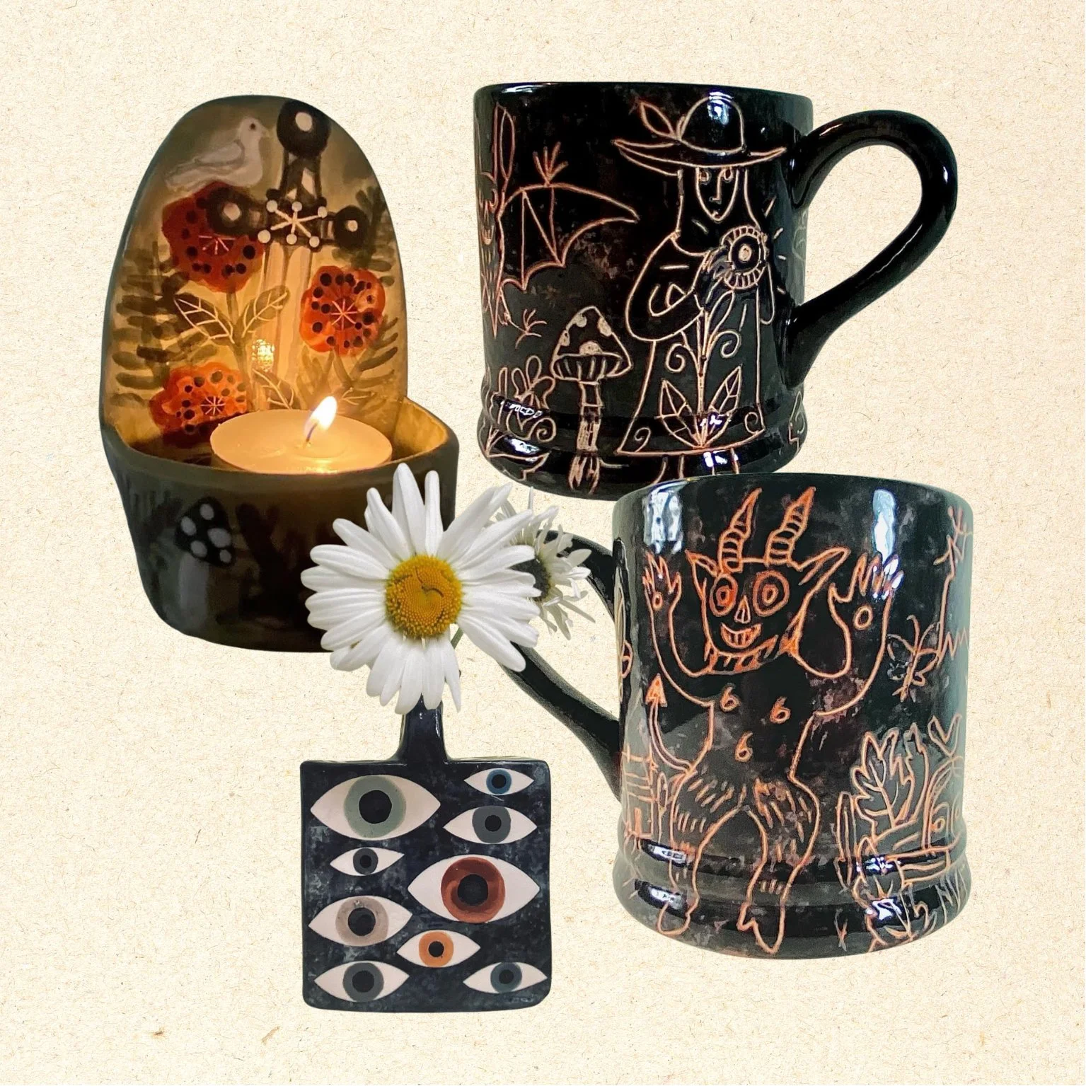 Decorative candles and mugs with witch and devil designs, a daisy, and an eye-themed hanging ornament.