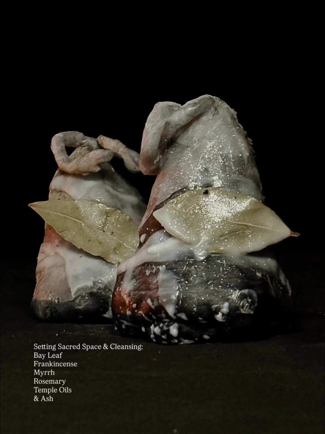 Arrangement of rocks, bay leaf, frankincense, myrrh, rosemary, temple oils, and ash on black background.