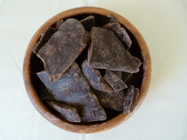 A small wooden bowl filled with dark, irregular ceramic shards on a white surface.