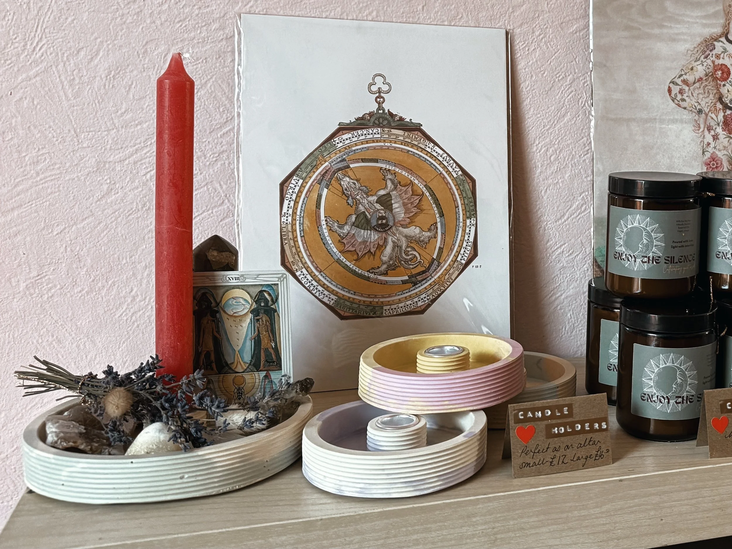 Decorative tabletop display with candles, a small box with religious artwork, a calendar or astrology chart, and labeled candle holders.