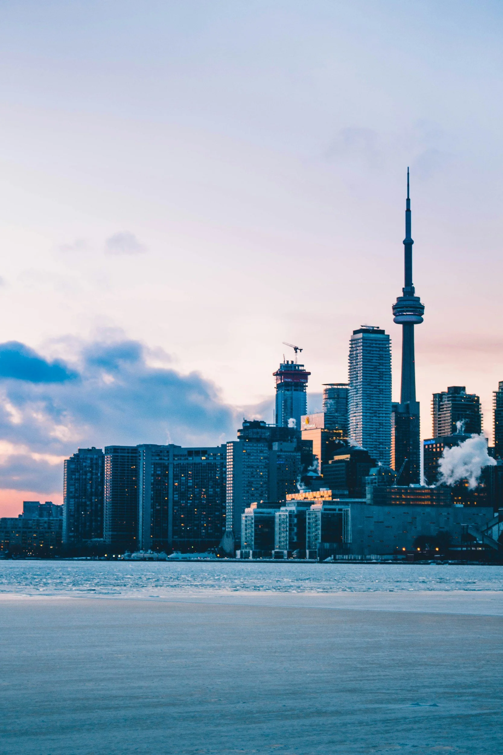 City skyline of Toronto with CN Tower, lakeside view during sunset.