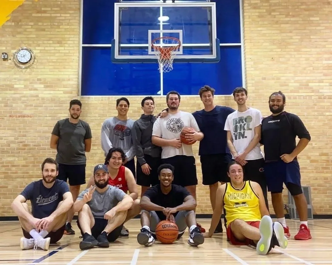 Group of young adults posing for a photo on a basketball court in front of a basketball hoop.
