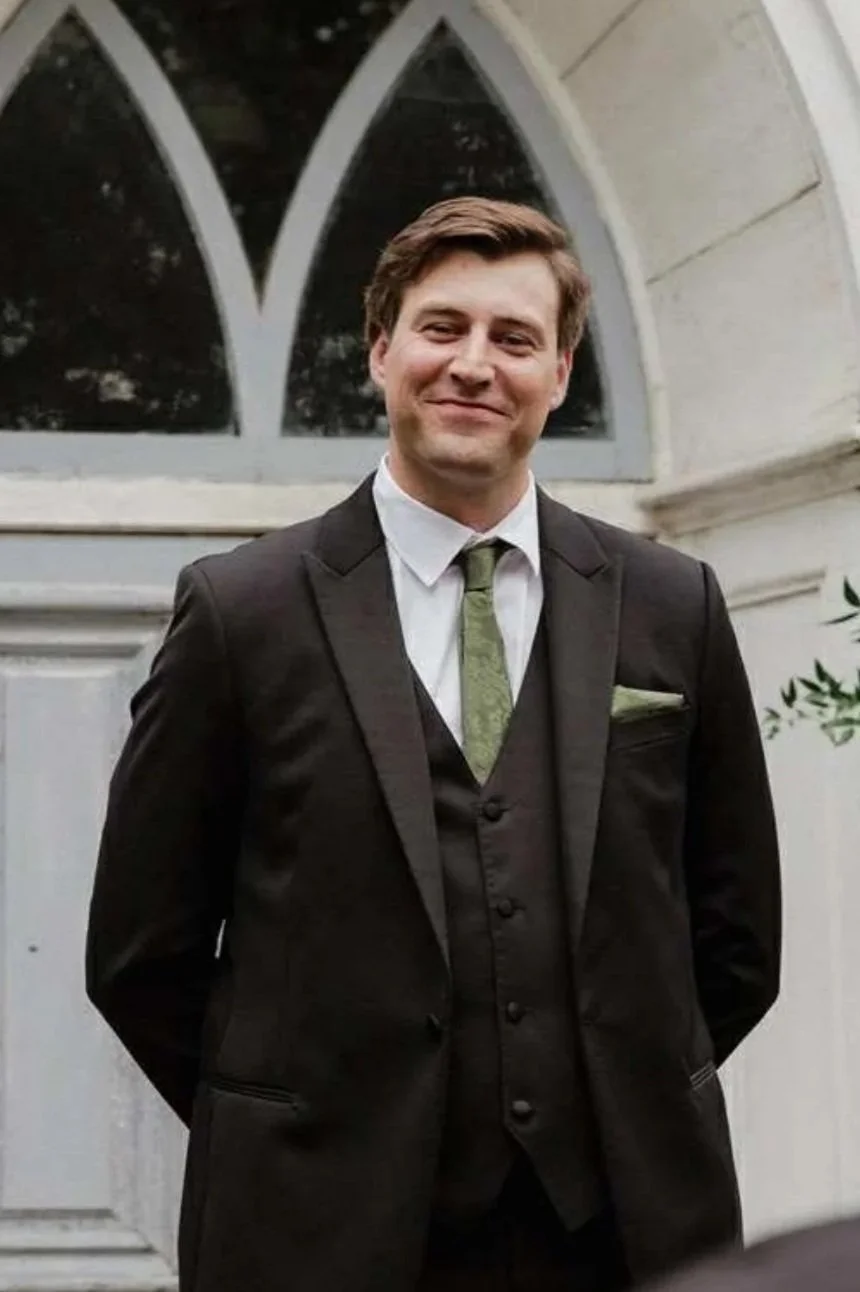 John MacLean posing in a handsome black suit at his friend's wedding.