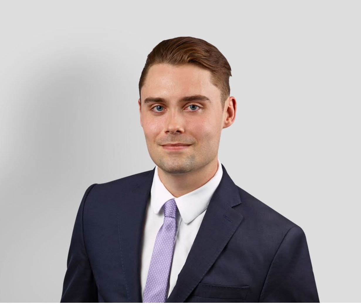 Portrait of a smiling young man in a suit and tie against a plain background.