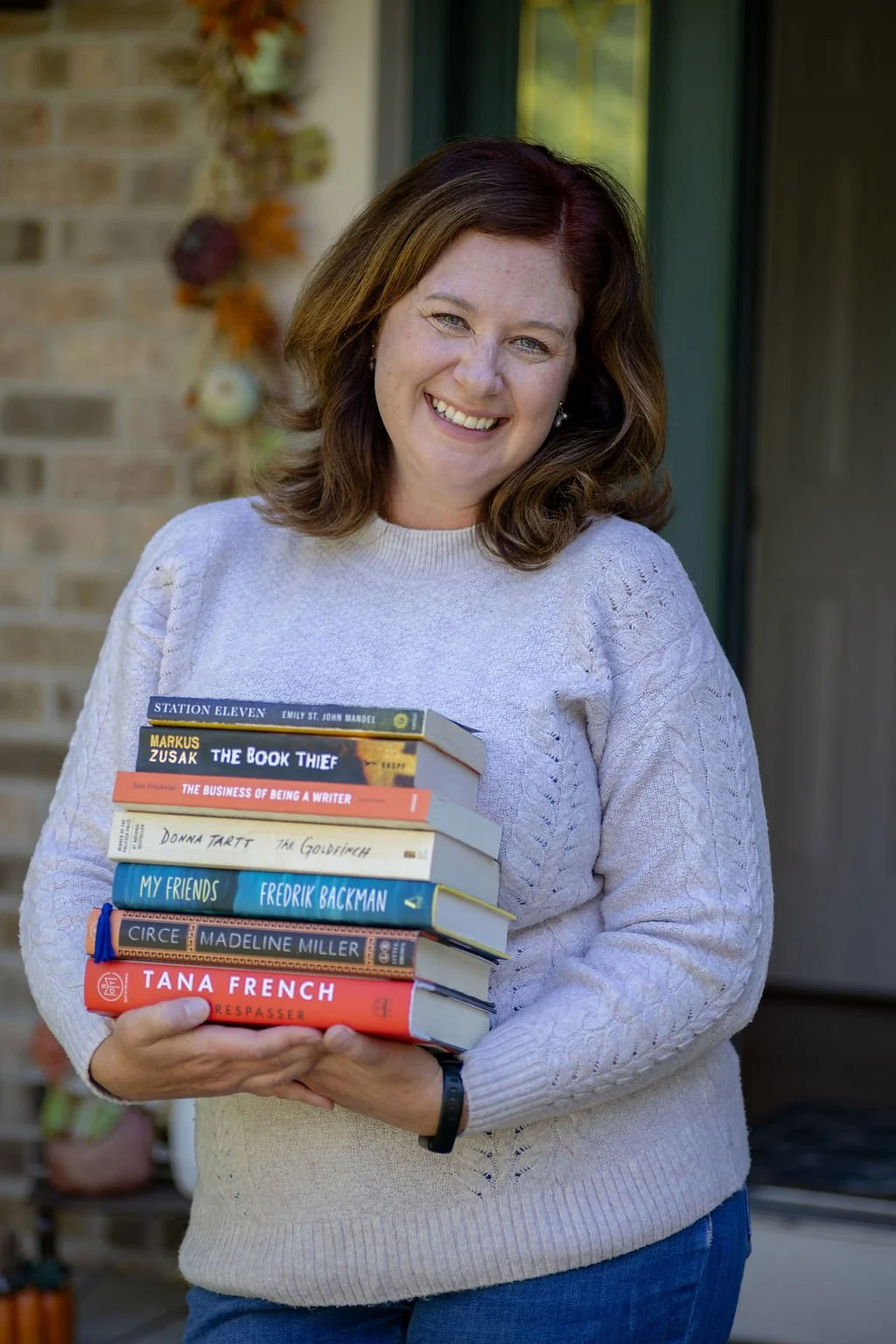 Fiction book coach Miranda Keskes is smiling while holding a stack of books outdoors.