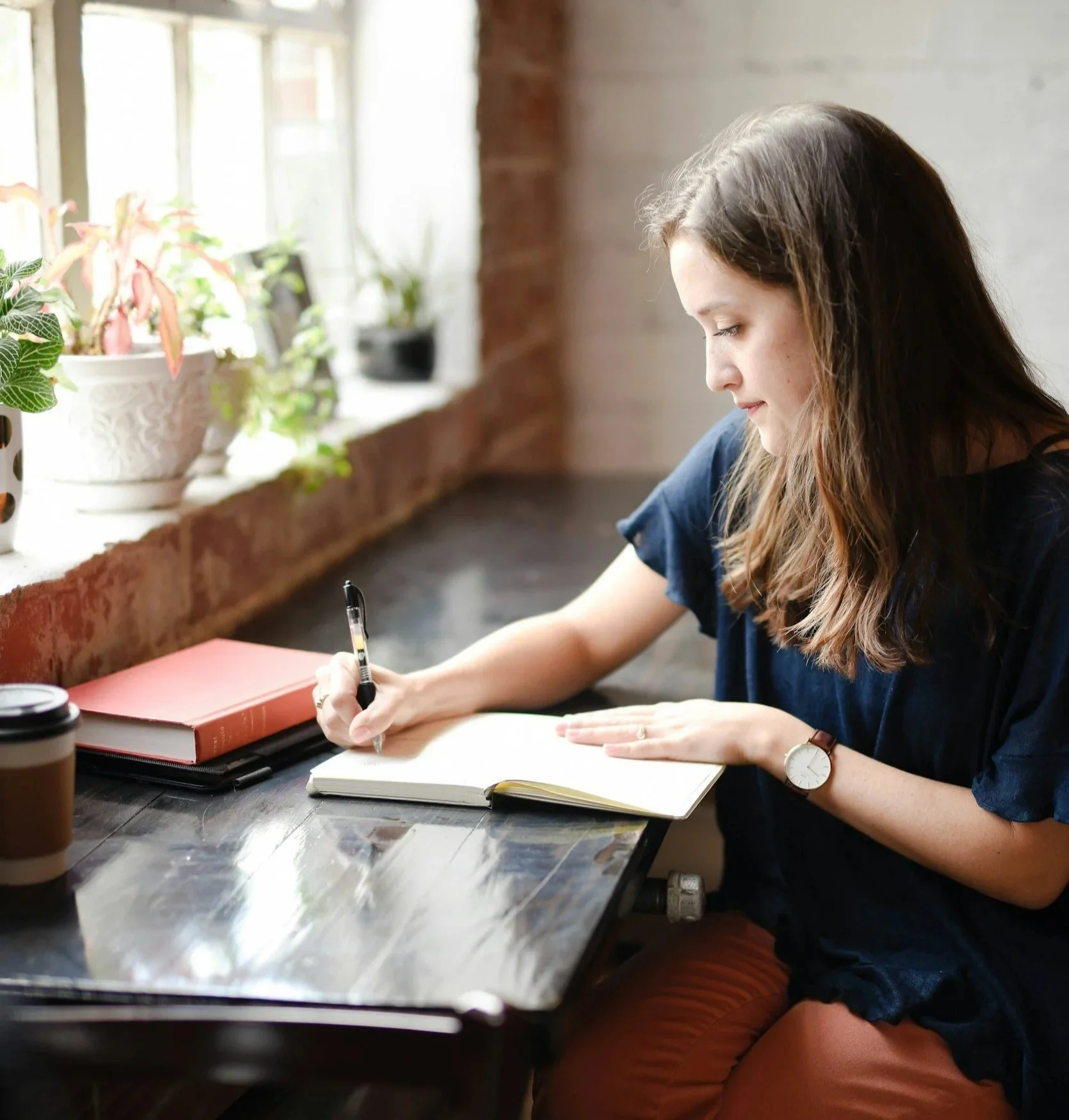 A woman with long brown hair writing in a notebook at a desk