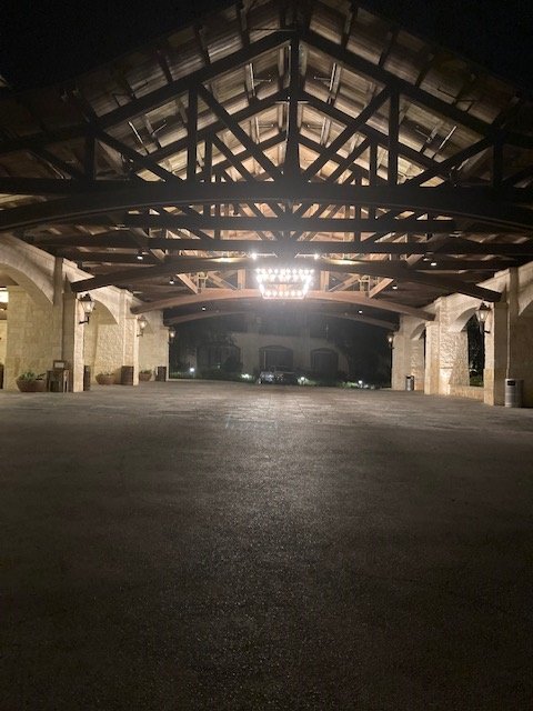 Empty outdoor parking area under a large covered structure at night with lights illuminating the space.
