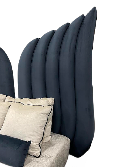 Close-up of a dark blue, scalloped, upholstered headboard with beige and black pillows on a bed.