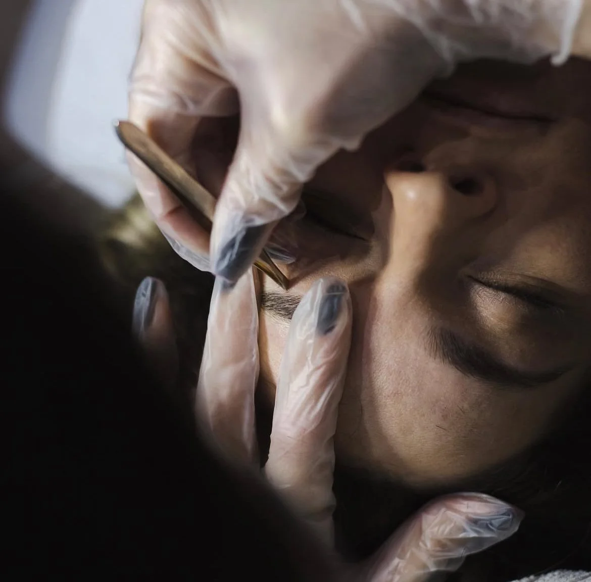 A person getting a nose piercing from a professional wearing gloves, with their eyes closed.