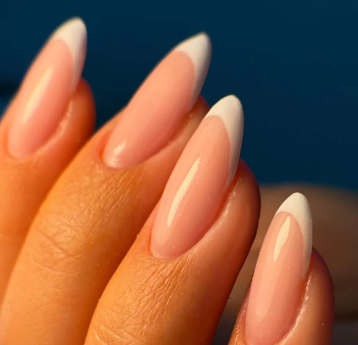 Close-up of well-manicured fingernails with natural pink color and white tips, displaying a French manicure style.