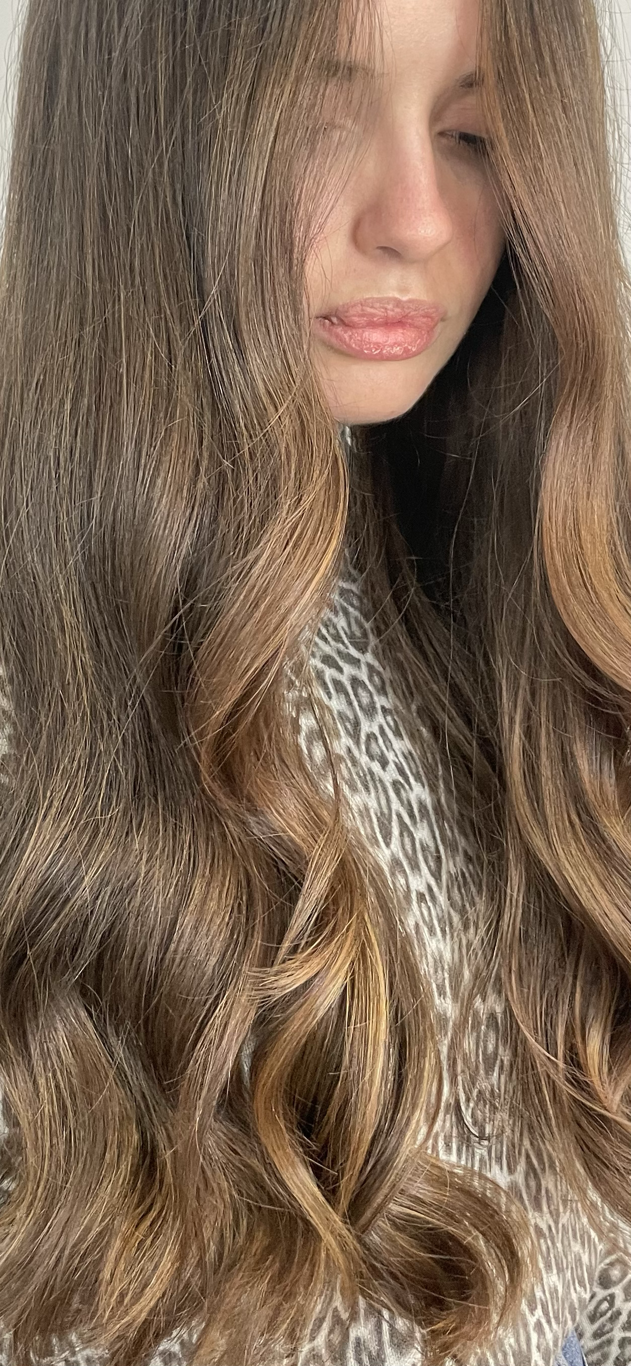 Close-up of a woman with long, wavy, light brown hair, slightly parted, wearing a leopard print top, with her lips slightly parted and eyes closed.