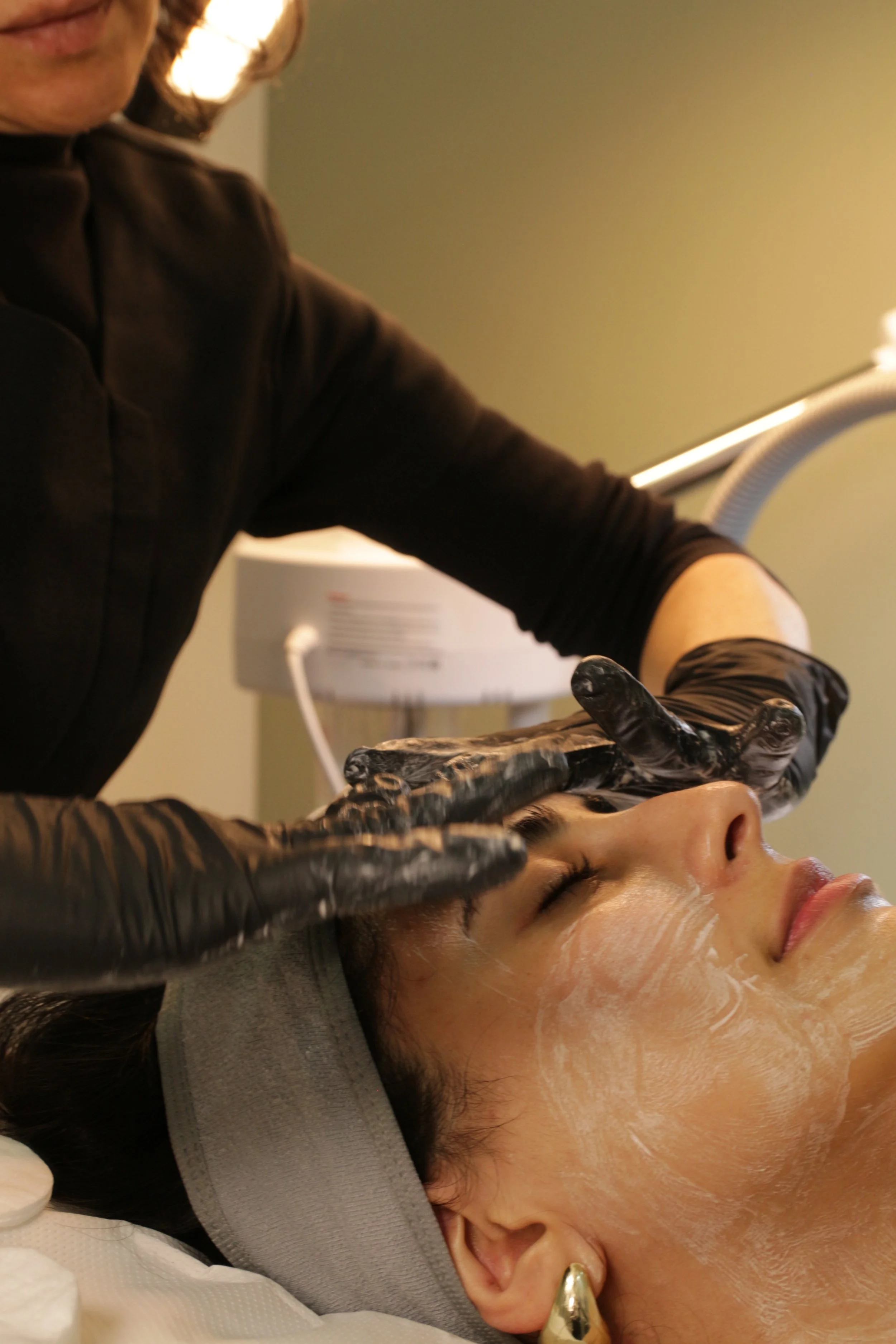 A woman receiving a facial treatment from an esthetician in a spa or clinic setting.