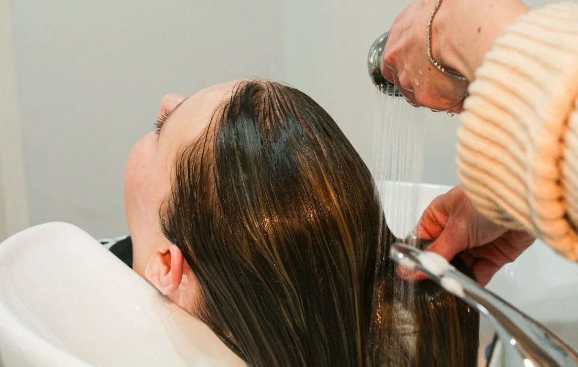 Person getting their hair washed at a salon sink with water pouring from a faucet.