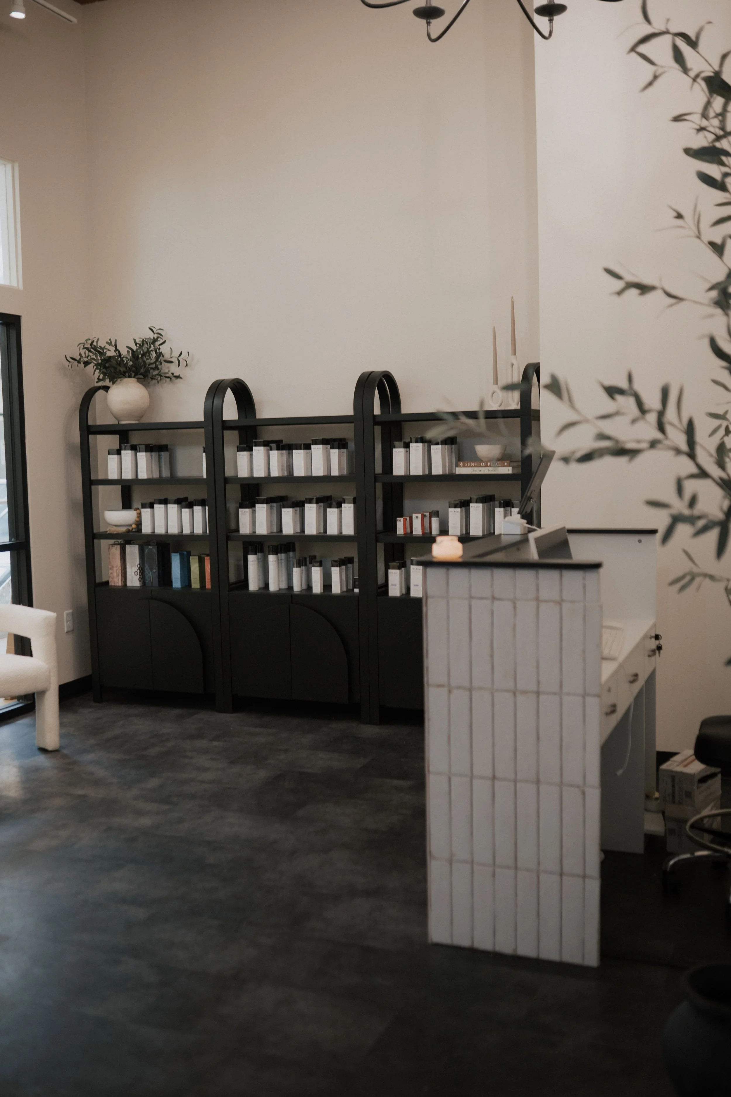 Interior of a modern office or reception area with black bookshelf, white wall, gray flooring, and a white tiled reception desk.