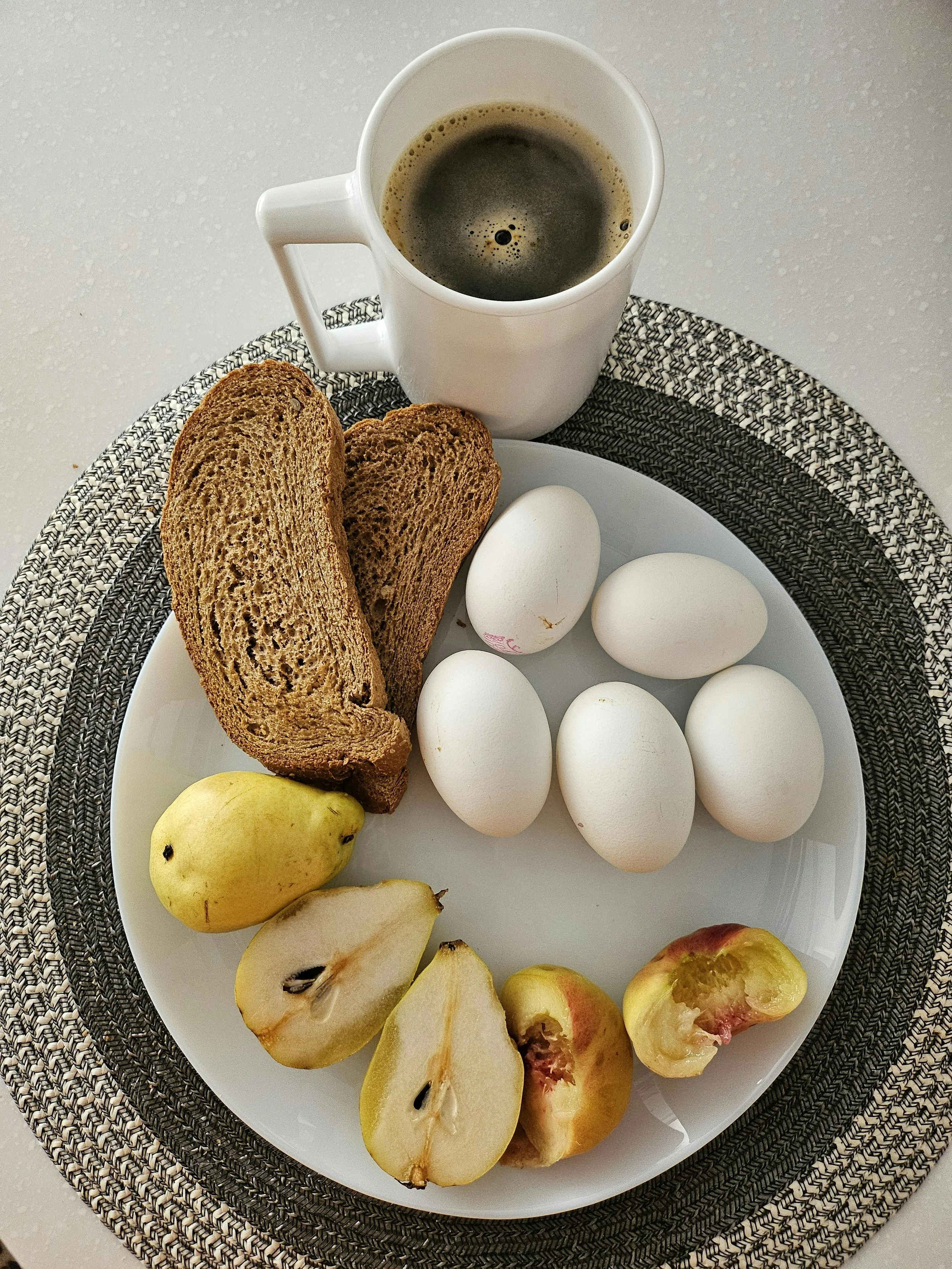 A white plate with six peeled pears, five eggs, and a sliced apple. The plate is on a black and white woven placemat.