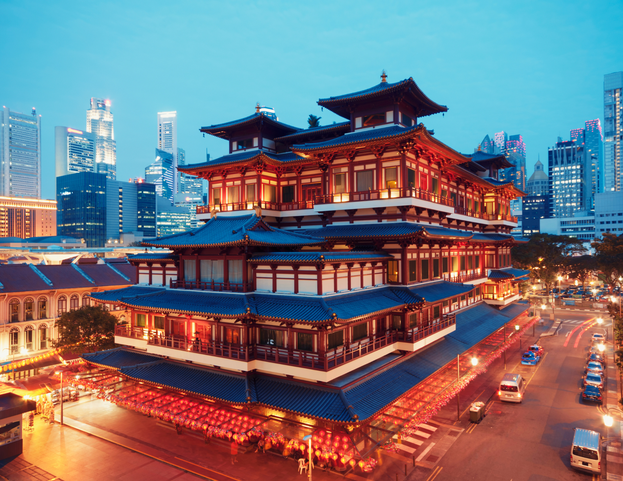 Traditional Chinese-style building with multiple tiers and ornate roof designs, illuminated at dusk in an urban setting with modern skyscrapers in the background.