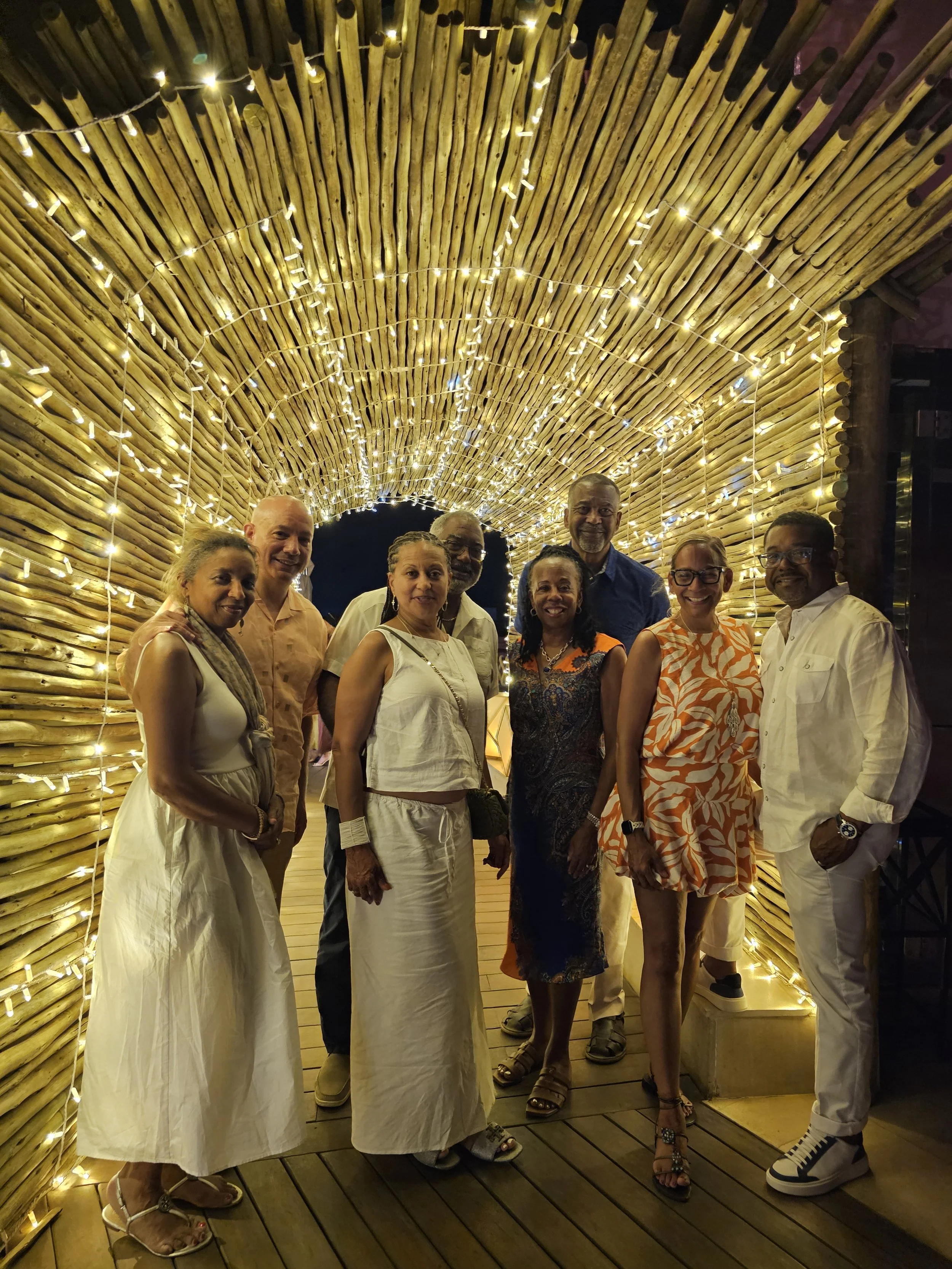 Group of people standing under a decorated bamboo arch with string lights at night.