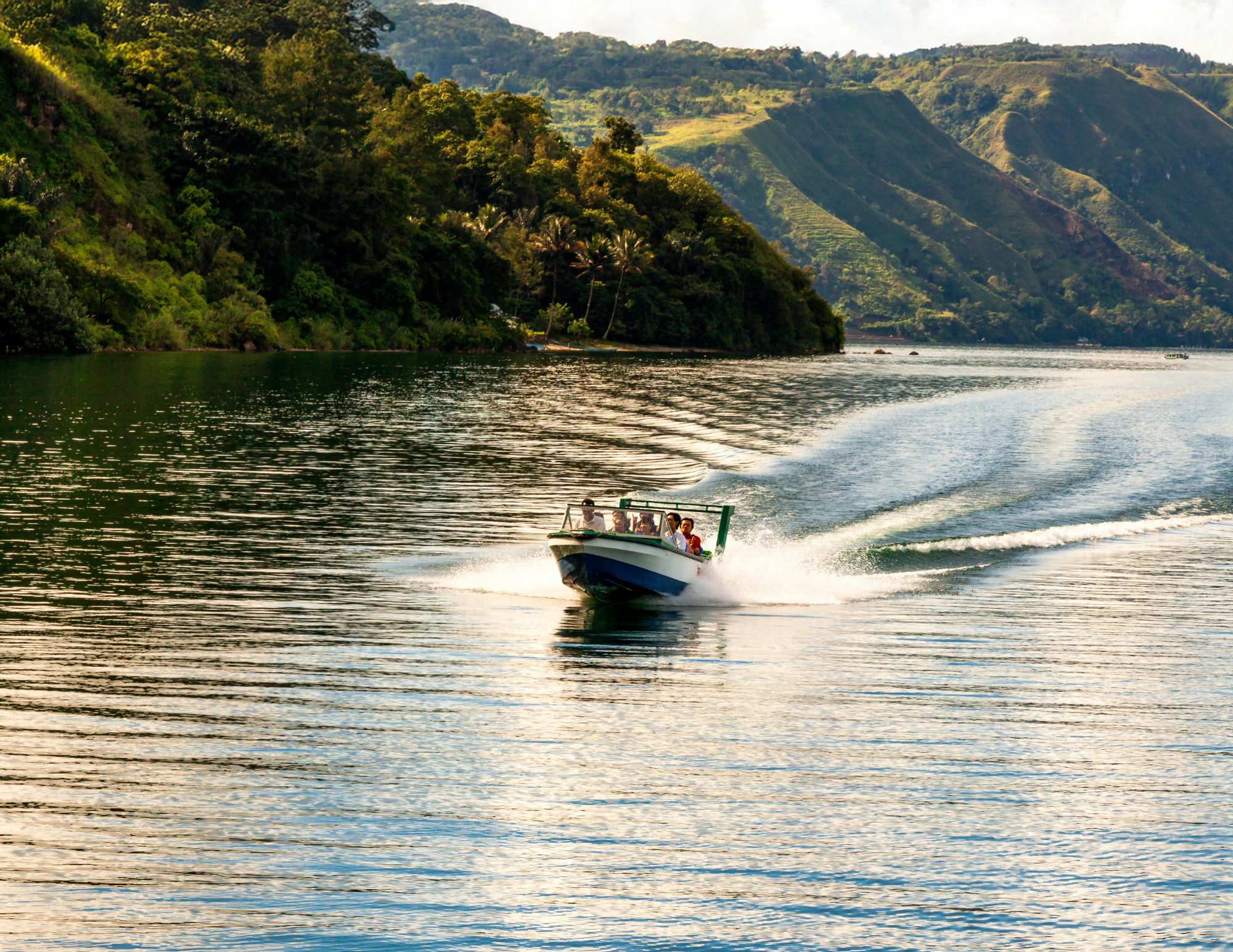 A boat speeding across a body of water with lush green hills in the background.