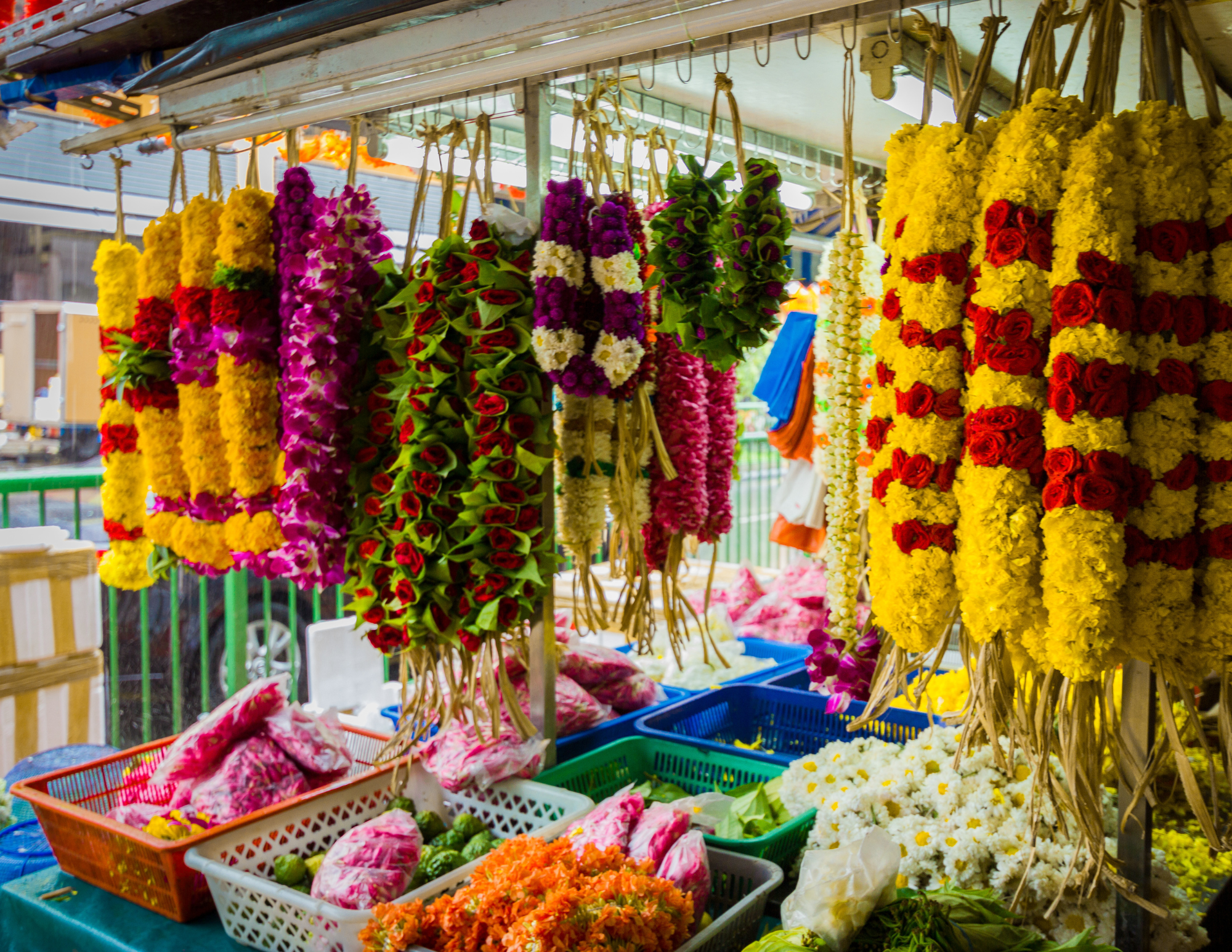 Colorful flower garlands hanging at a street stall, with baskets of flowers and other items on table below.