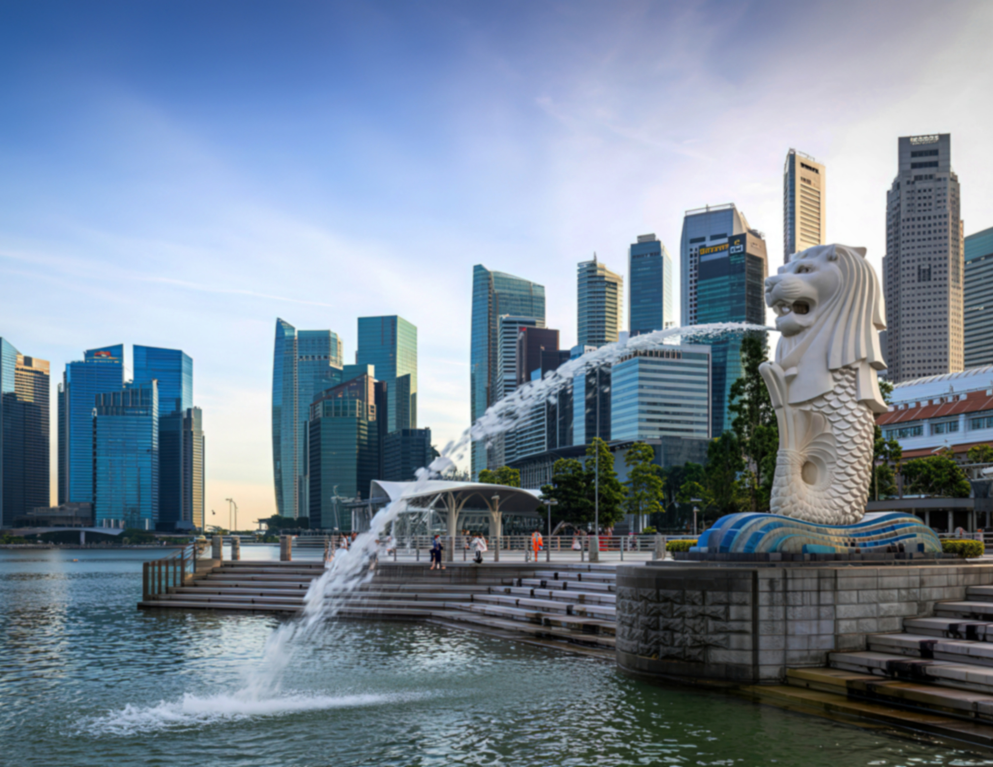 Singapore's Marina Bay skyline with the Merlion statue in the foreground, overlooking the water and modern skyscrapers.