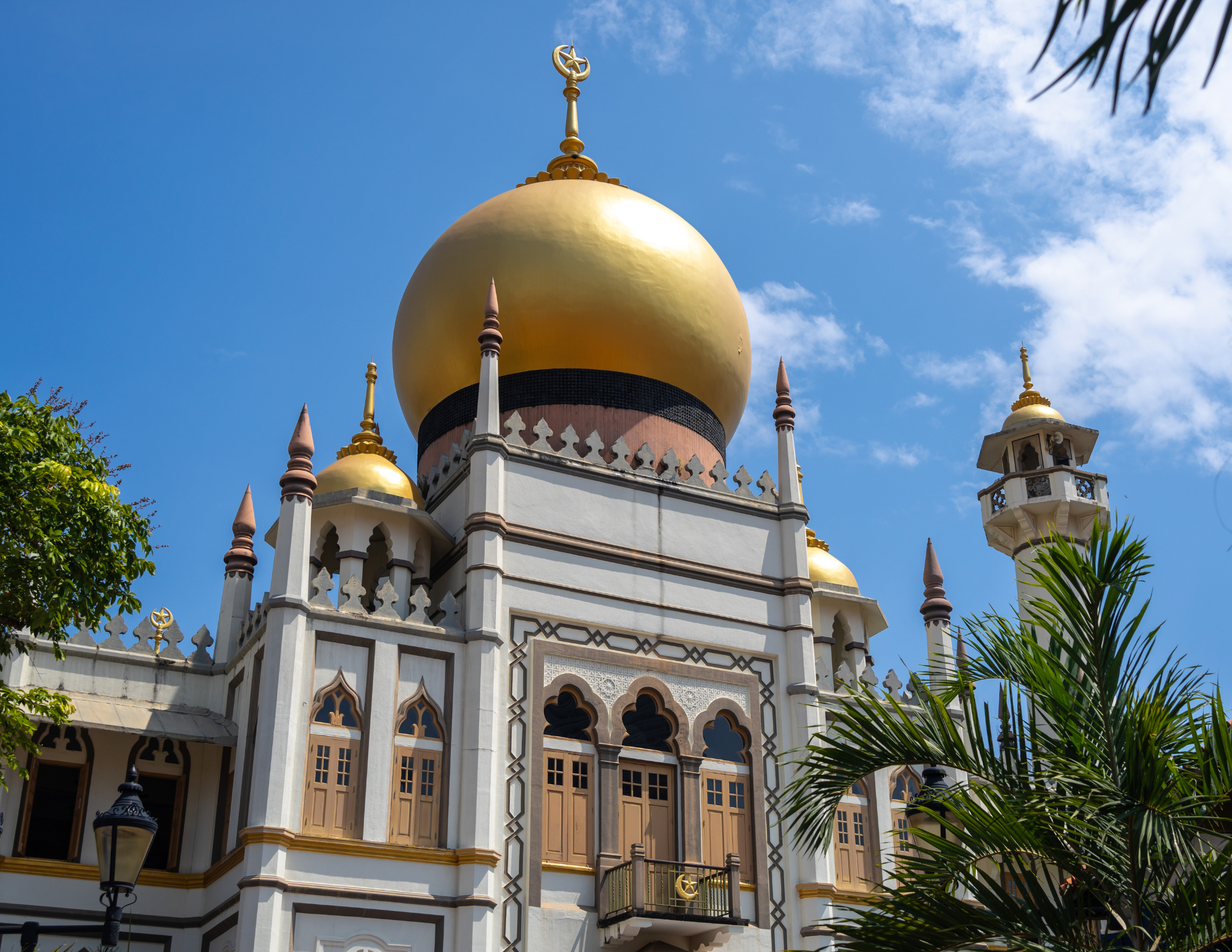 A mosque with a large gold dome, multiple smaller domes, and minarets against a blue sky with some clouds.