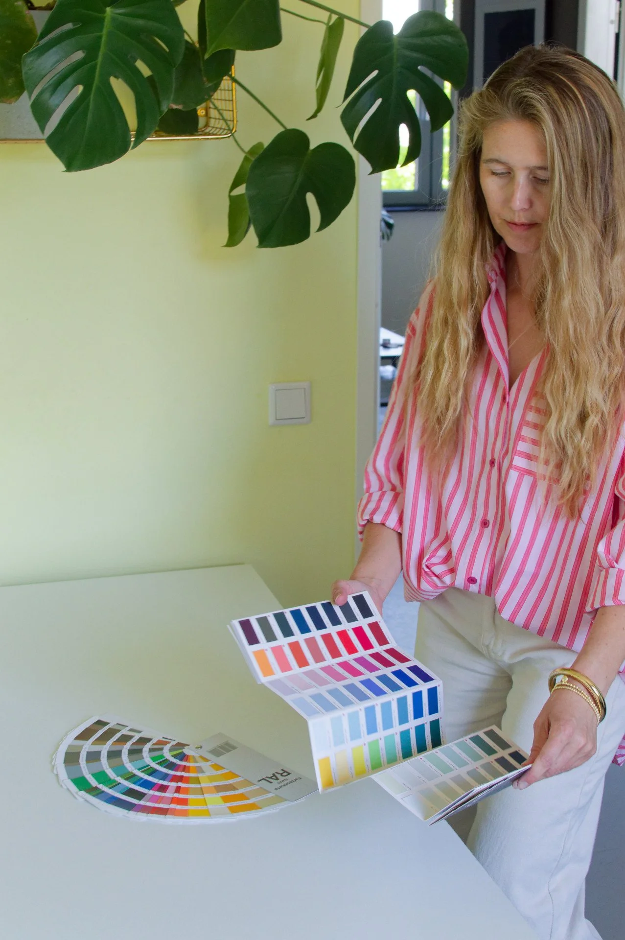 Woman looking at color swatch book in a room with green plants and yellow wall