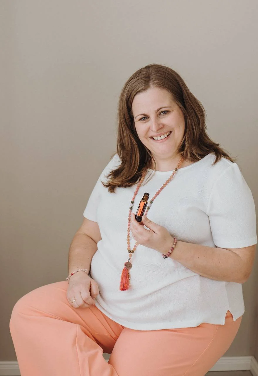 Eine lachende Frau mit braunen Haaren, die ein Fläschchen ätherisches Öl hält.