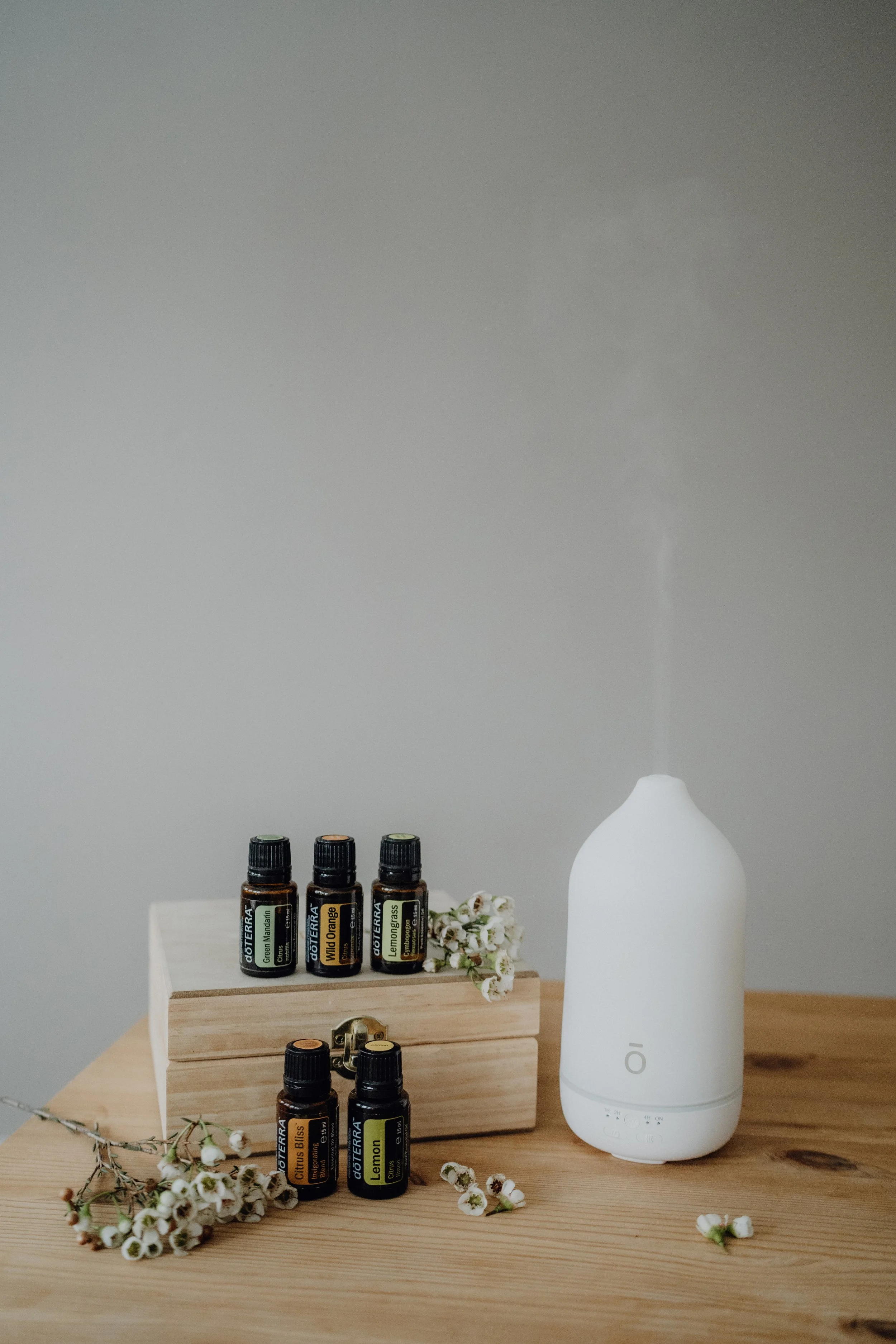 Ätherische Öle auf Holzbox, weißer Diffusor, kleine weiße Blumen auf Holz Tisch.