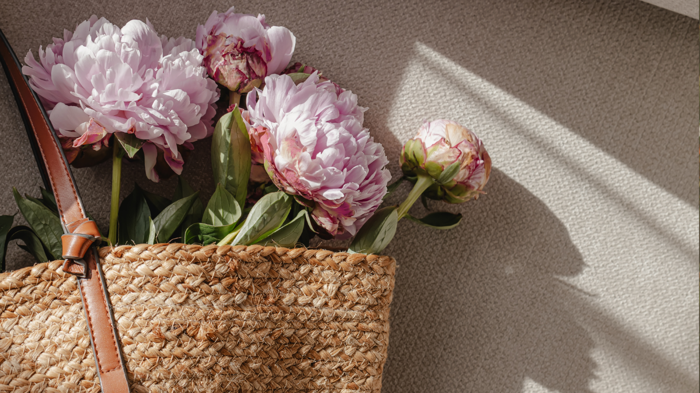Strauß aus pinken Pfingstrosen in einem geflochtenen Korb auf einem Teppichboden, mit Sonnenlicht und Schatten.