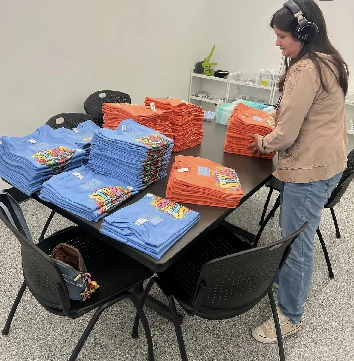 Stack of custom printed shirts in different colors on a worktable in a print shop.