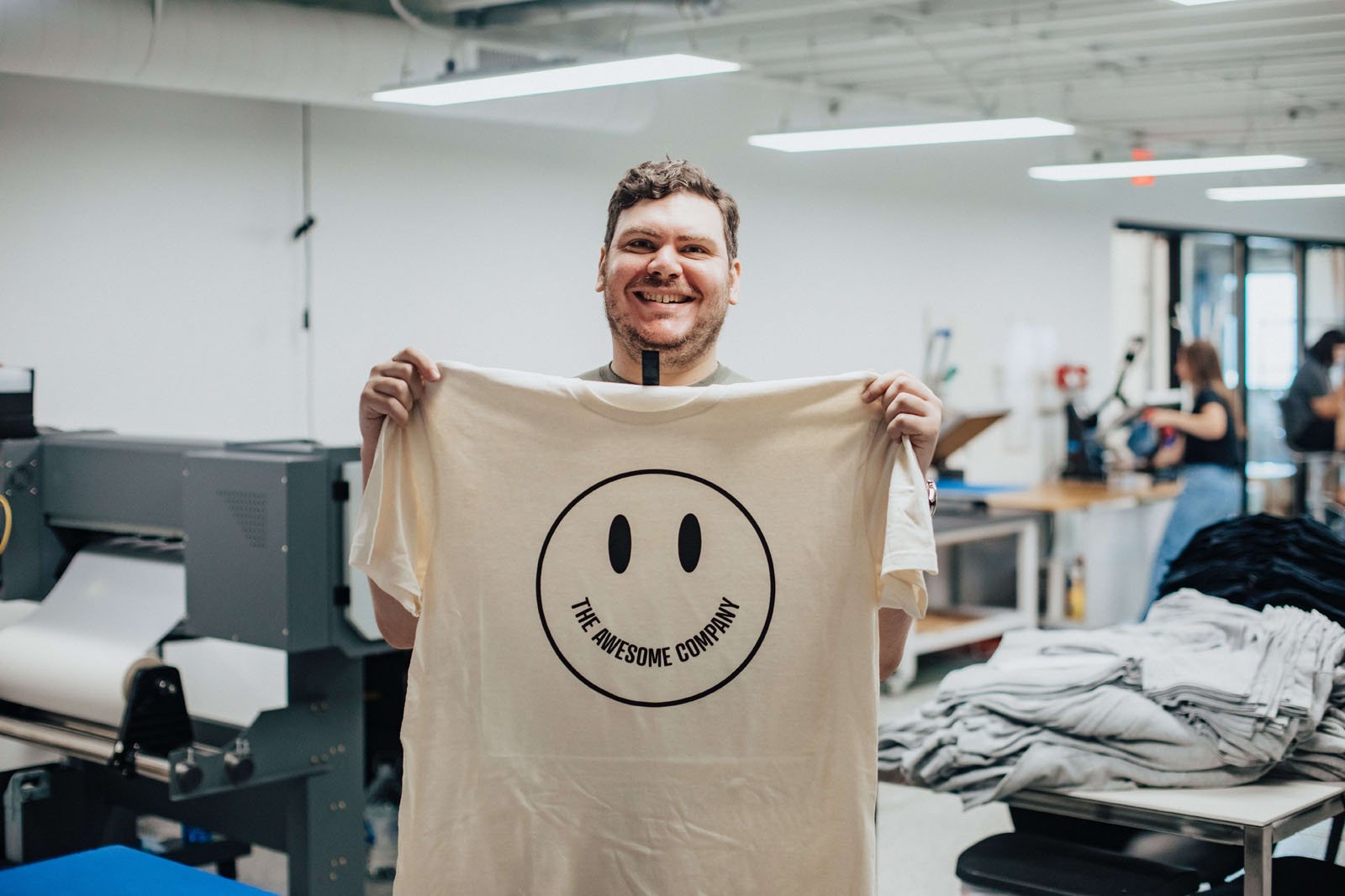 Autistic employee holding up a finished garment with a big smile on his face..