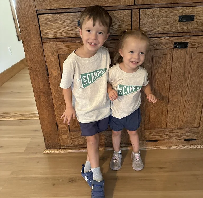 Two smiling siblings posing together wearing their matching custom annual camping t-shirts.
