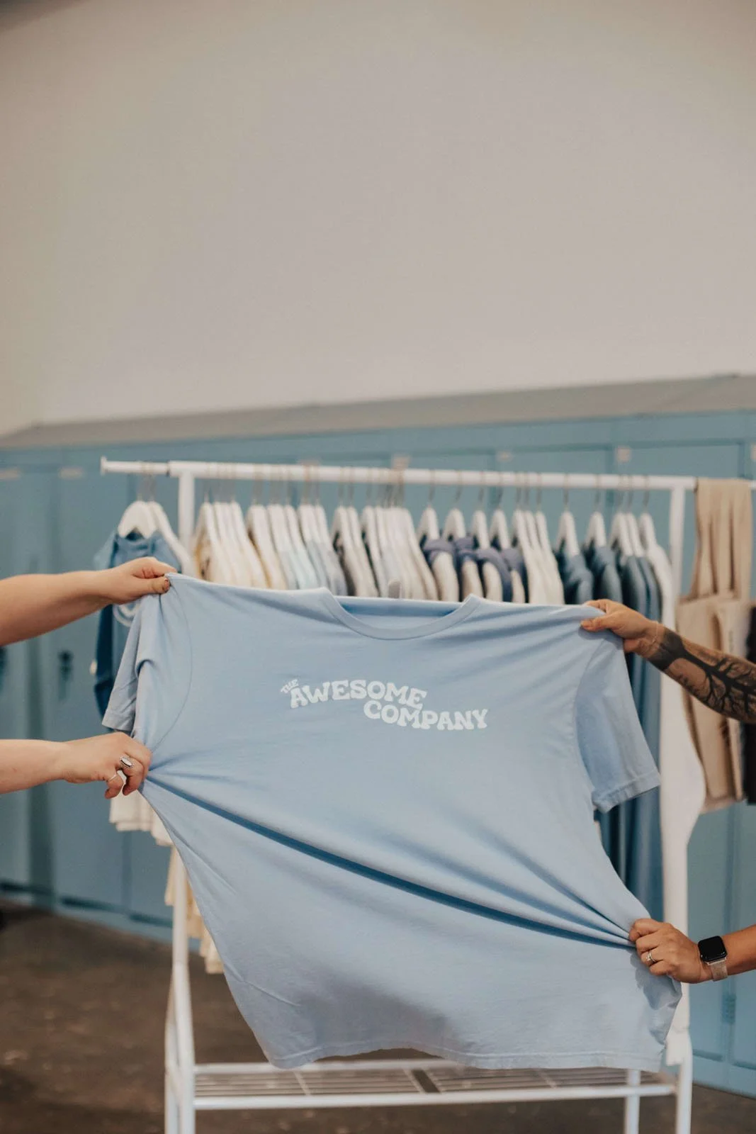 The Awesome Company T-shirt being held by two people.